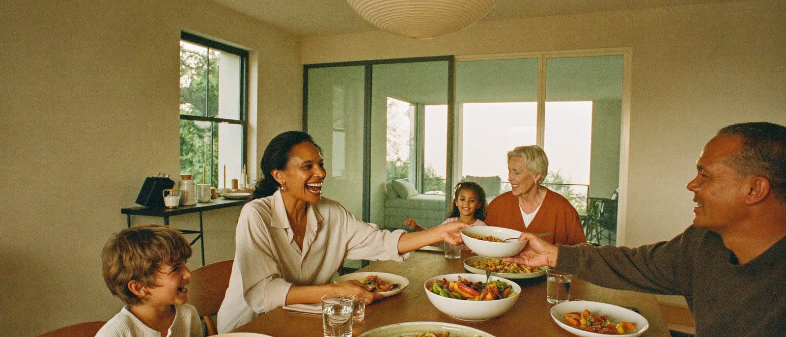 Three generations of a family laughing together around a kitchen table at dinner